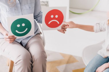 cropped shot of psychologist showing happy and sad emotion faces cards to child clipart