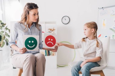 Yetişkin psikolog mutlu ve hüzünlü duygu gösterilen kartlar için çocuk yüzleri