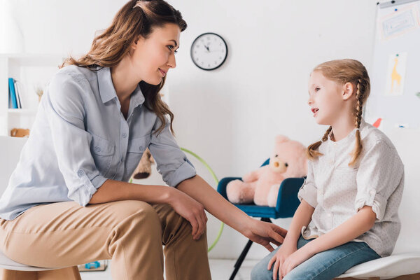beautiful adult psychologist talking with little patient in office