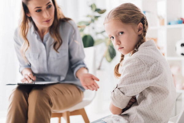 psychologist talking to angry child with crossed arms while she looking at camera