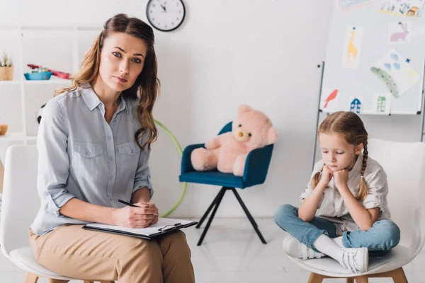 Adult Psychologist Clipboard Sitting Little Depressed Child Office Looking Camera — Stock Photo, Image