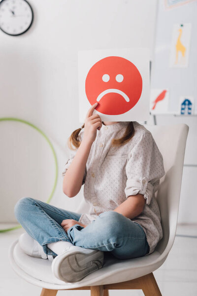 little child sitting on chair and covering face with sad face symbol