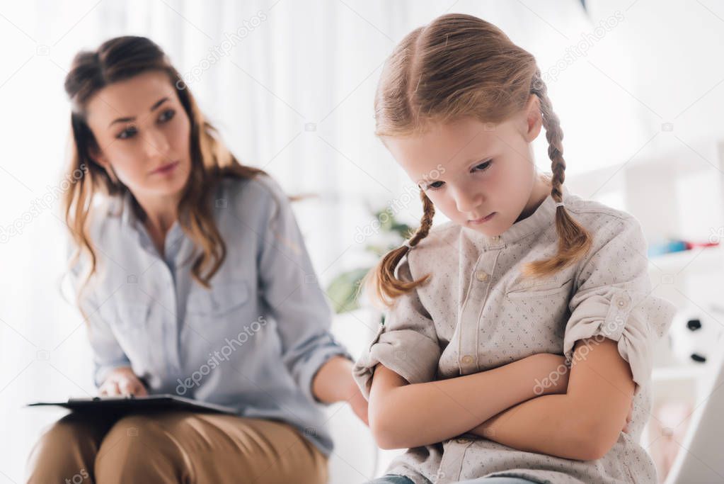 adult psychologist talking to depressed child with crossed arms