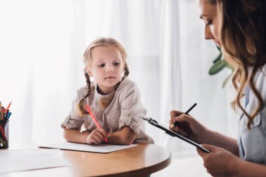psychologist writing in clipboard while sitting near little drawing child clipart