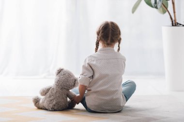 rear view of little child sitting on floor with her teddy bear toy clipart