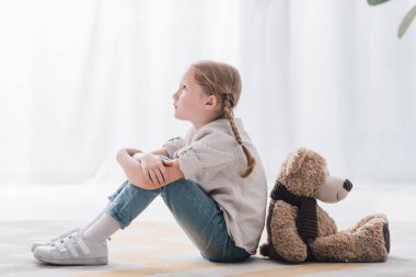 side view of thoughtful little child sitting on floor back to back with teddy bear clipart