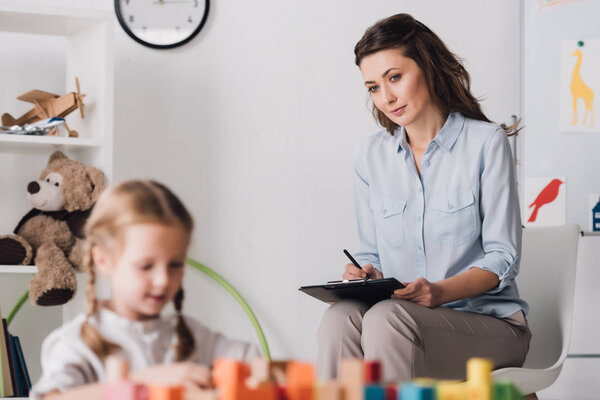 little child playing with blocks while psychologist sitting blurred on background
