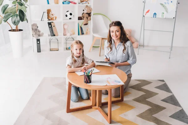 Gelukkig Psycholoog Met Klembord Zitten Buurt Van Klein Kind Terwijl — Stockfoto