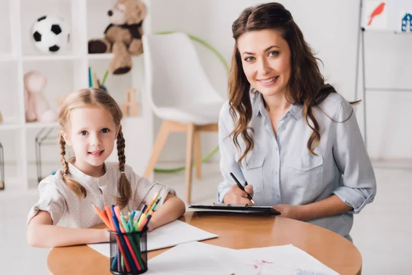 Psicologa Sorridente Con Appunti Seduta Vicino Bambino Mentre Disegna Con — Foto Stock