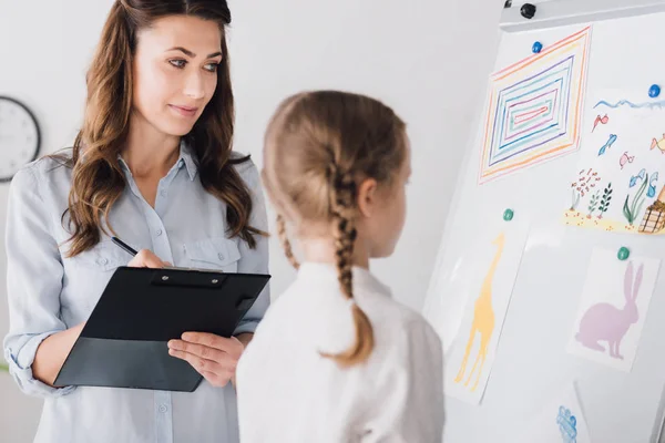 Psicólogo Escribiendo Portapapeles Mientras Niño Mirando Pizarra Blanca Con Varios — Foto de Stock