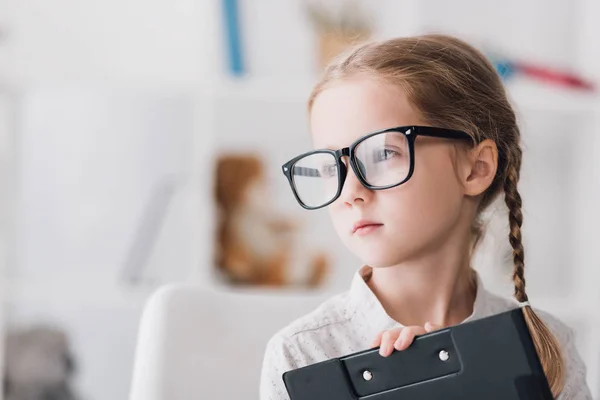 クリップボードを押しながらよそ見の眼鏡で 幼い子供のクローズ アップの肖像画 — ストック写真