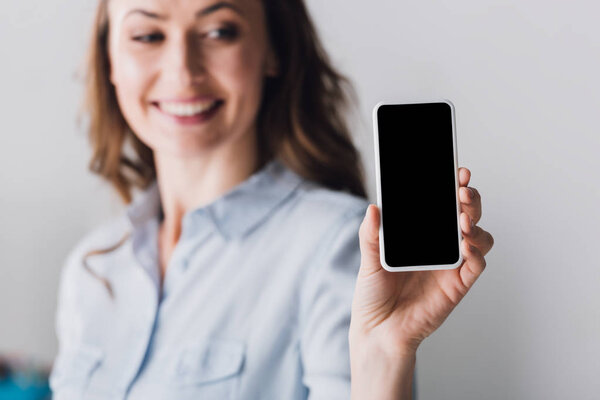 close-up portrait of happy adult woman in shirt showing smartphone with blank screen at camera