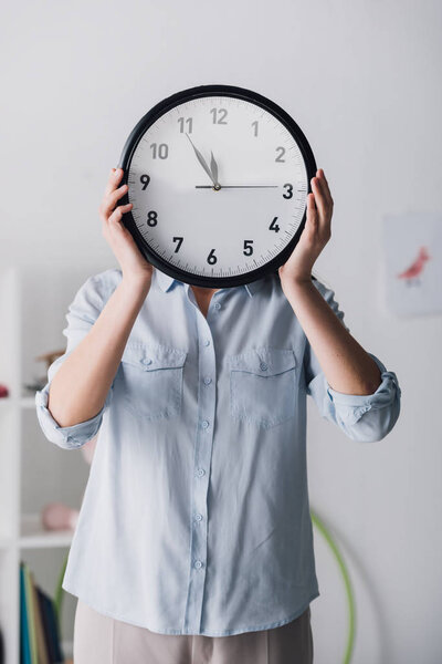 close-up portrait of woman in shirt covering face with clock