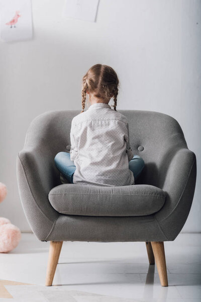 rear view of lonely little child sitting in armchair in front of white wall