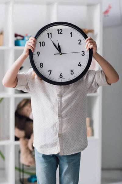 little child covering face with big clock