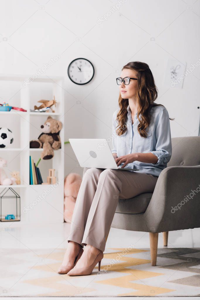 child psychologist sitting in armchair with laptop and looking away
