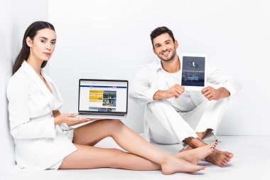gadget'lar ile katta oturan ve tumblr app ve rezervasyon web sitesi ekranlarında gösterilen toplam beyaz yetişkin çift