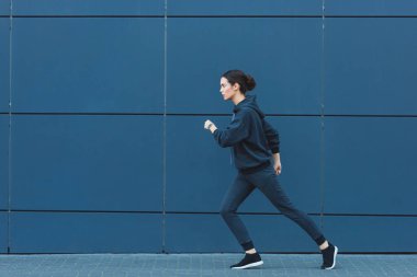 active adult sportswoman jogging in sportswear near building  clipart