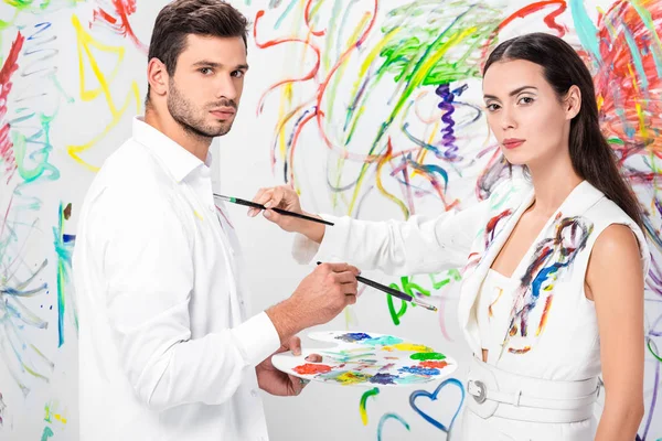 studio shot of couple in total white drawing on clothes with painbrushes