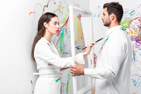 attractive adult woman drawing on clothes while man holding frame