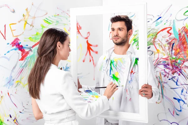 attractive adult woman drawing on clothes while man holding frame