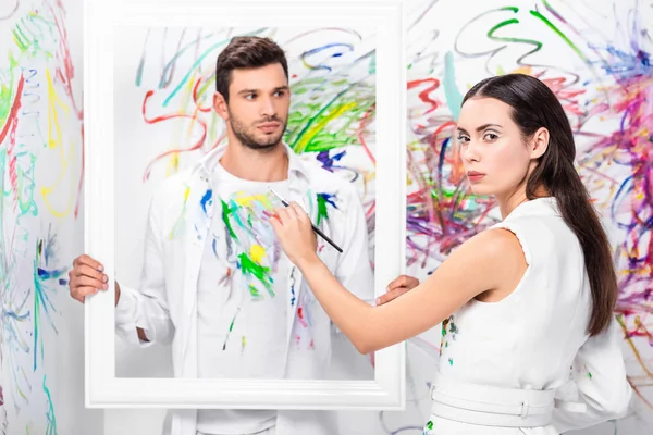 Close Adulto Homem Segurando Moldura Branca Enquanto Mulher Pintando Roupas — Fotografia de Stock