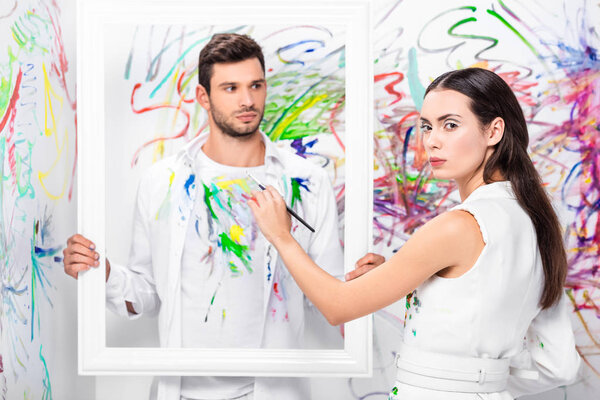 крупным планом взрослого мужчины с белой рамкой в то время как женщина рисует одежду
