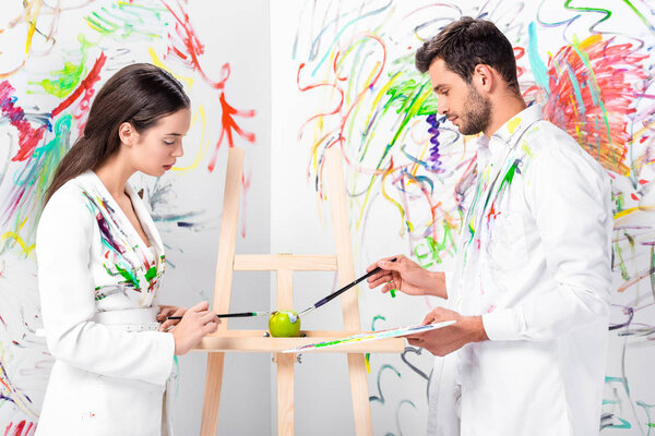 Взрослая пара рисует зеленое яблоко на мольберте
 