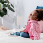 Curly enfant afro-américain assis sur le lit et souriant