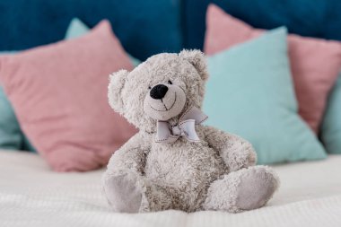 Close up horizontal view of teddy bear sitting on the bed with pillows on background clipart