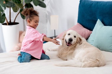 adorable african american child sitting on the bed and shows smartphone screen to dog clipart