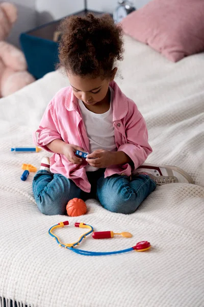 卷曲非洲裔美国孩子在床上玩玩具听诊器 — 图库照片