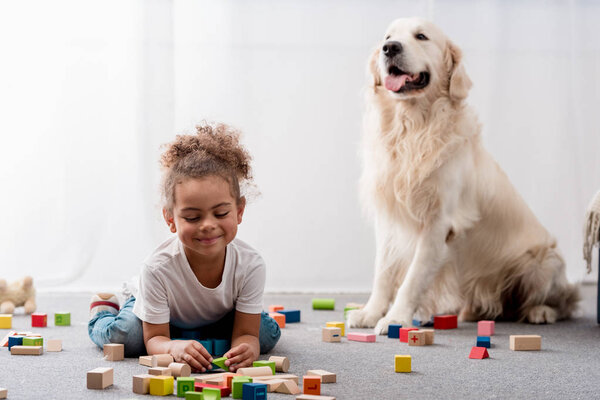 Adorable african american child playing with toy cubes and dog 