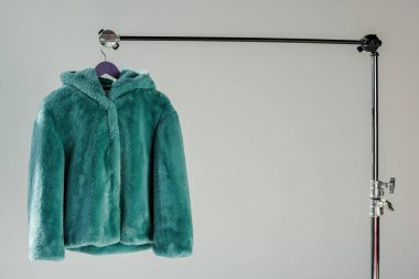 fluffy green faux fur coat hanging on rack at grey background with sunbeams clipart