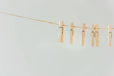 close up of raw of wooden clothespins hanging on clothesline isolated on grey clipart