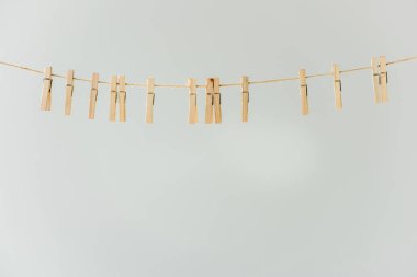 close up of raw of wooden clothespins hanging on clothesline isolated on grey clipart