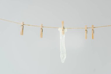 raw of wooden clothespins with white condom hanging on clothesline isolated on grey clipart