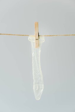 close up of white condom hanging on clothesline with pin isolated on grey clipart