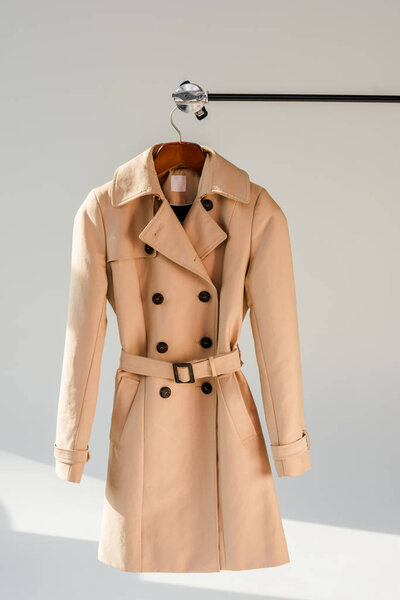 beige trench coat with belt and black buttons on hanger