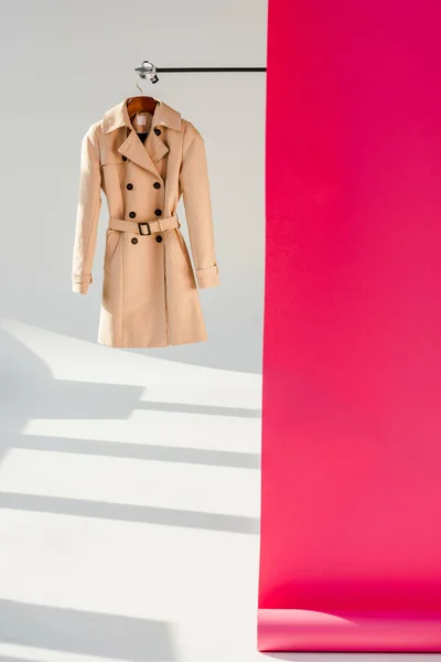 elegant beige trench coat on hanger with pink wallpaper