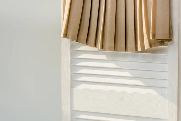 close up of beige pleated skirt hanging on white room divider isolated on grey