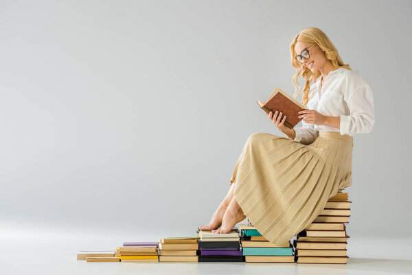 attractive smiling barefoot woman in glasses sitting on steps made of books  