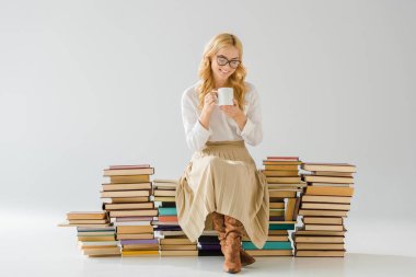 çekici kadın kahve içme ve retro kitap yığını üzerinde oturan gözlüklü