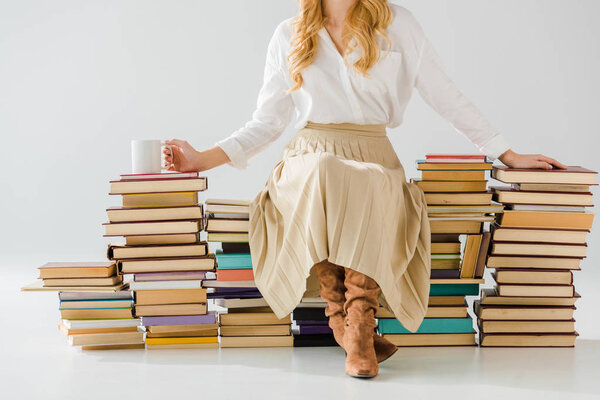 close up of adult woman sitting on a pile of books with cup
