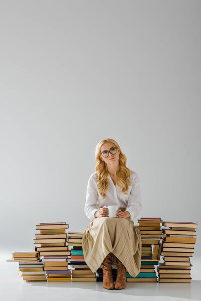 attractive woman in glasses with cup sitting on pile of retro books