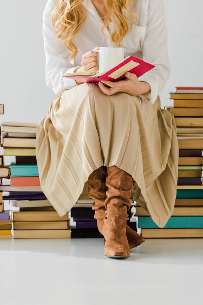 close up of woman drinking coffee, reading and sitting on a pile of books
