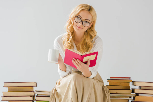 close up of woman drinking coffee, reading and sitting on books