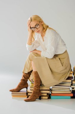retro kitap yığını üzerinde oturan gözlüklü yorgun sarışın kadın