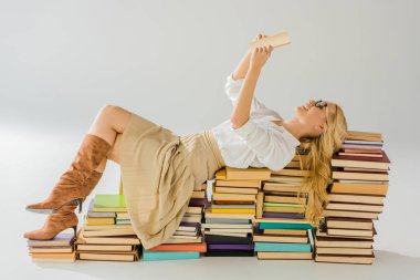 beautiful blonde woman in glasses reading and laying on pile of retro books clipart