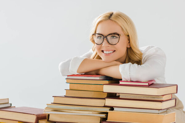 smiling blonde adult woman in glasses with books isolated on grey